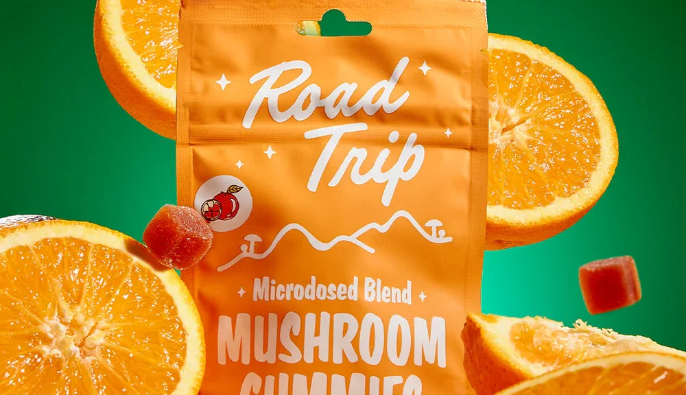 Road Trip microdosed mushroom gummies orange-flavored bag surrounded by fresh orange slices on green background